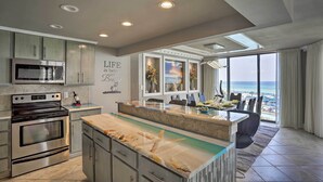 A modern kitchen with a large island, built-in oven, and a view of the beach through large windows.
