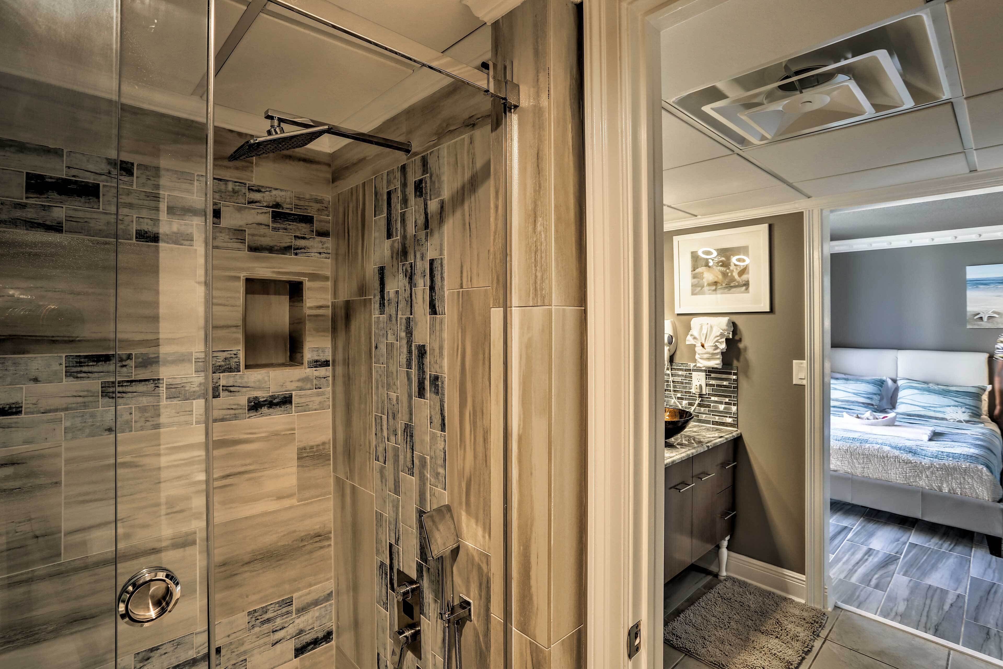 A modern bathroom with a shower, a vanity with a sink, and a bed in the adjacent room.