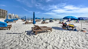A beach with rows of wooden lounge chairs and blue umbrellas, some with bags and items on them.