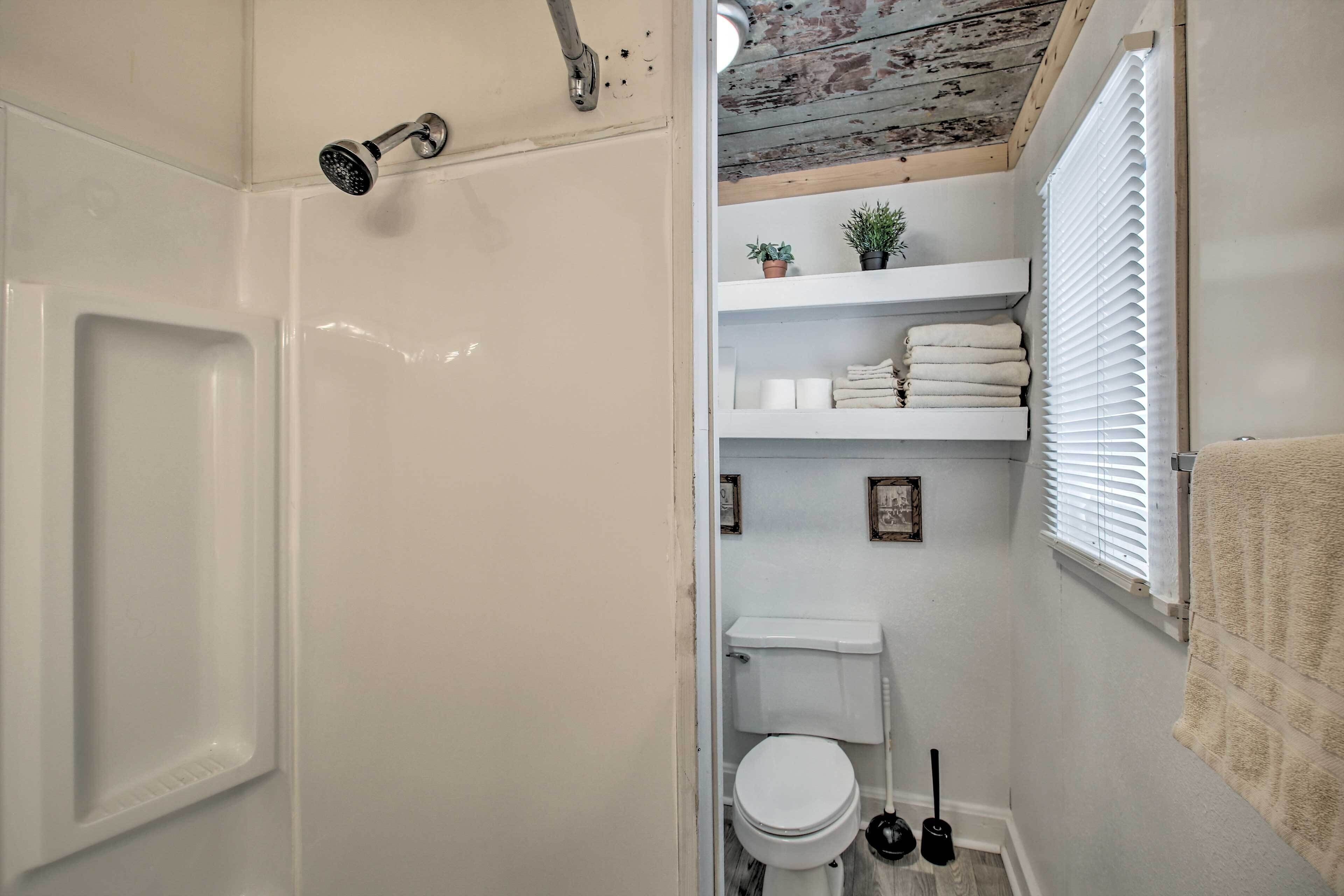 Une petite salle de bain avec une douche, des toilettes et des étagères où sont rangées des serviettes et des plantes.