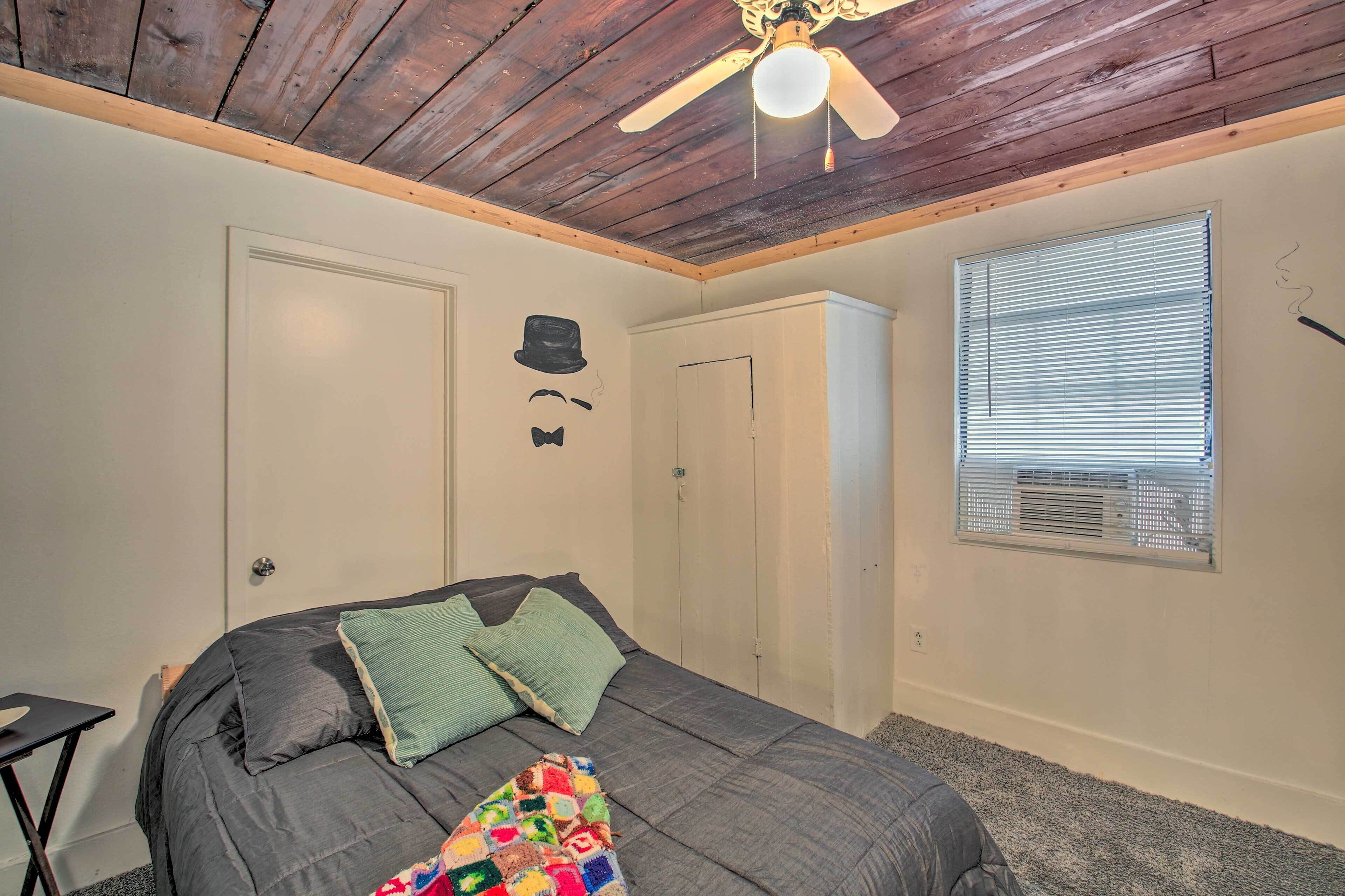 Un dormitorio con cama, ventilador de techo, ventana con persianas y puerta.