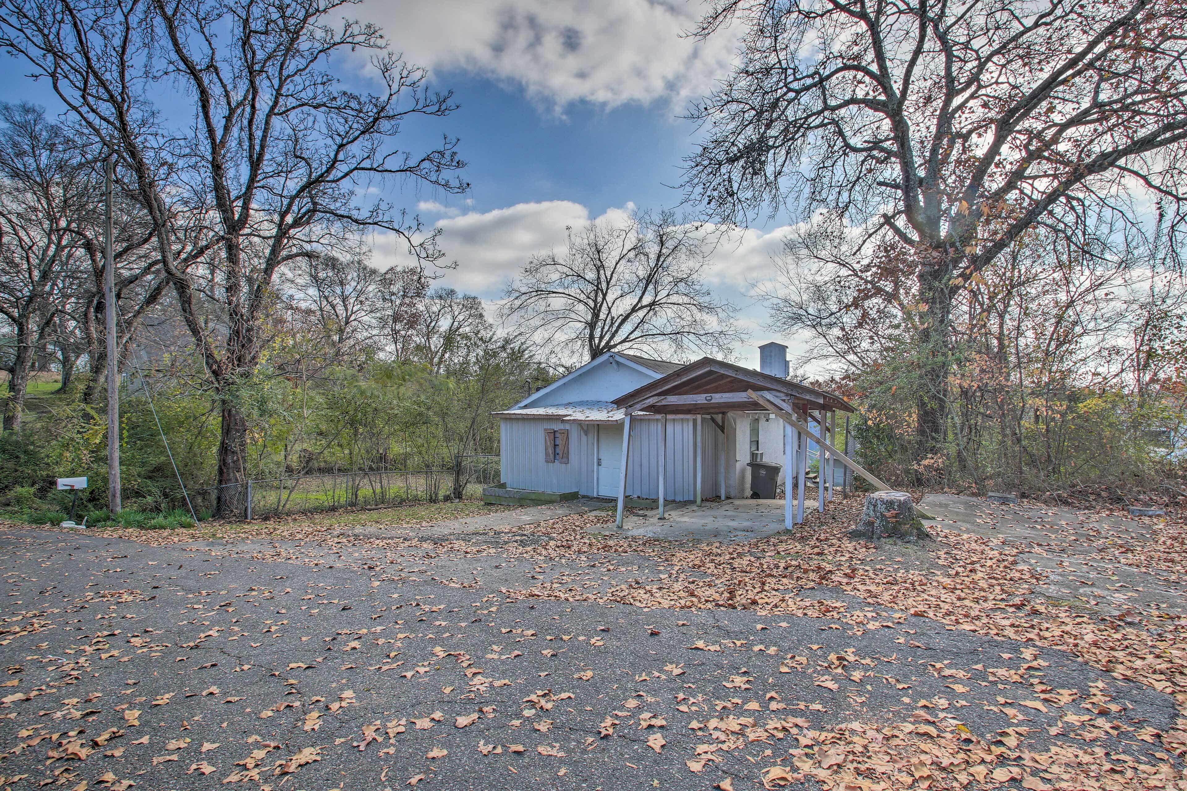 A small, single-story house with a porch, surrounded by trees and a gravel driveway.