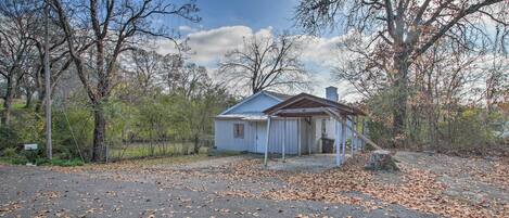 A small, single-story house with a porch, surrounded by trees and a gravel driveway.
