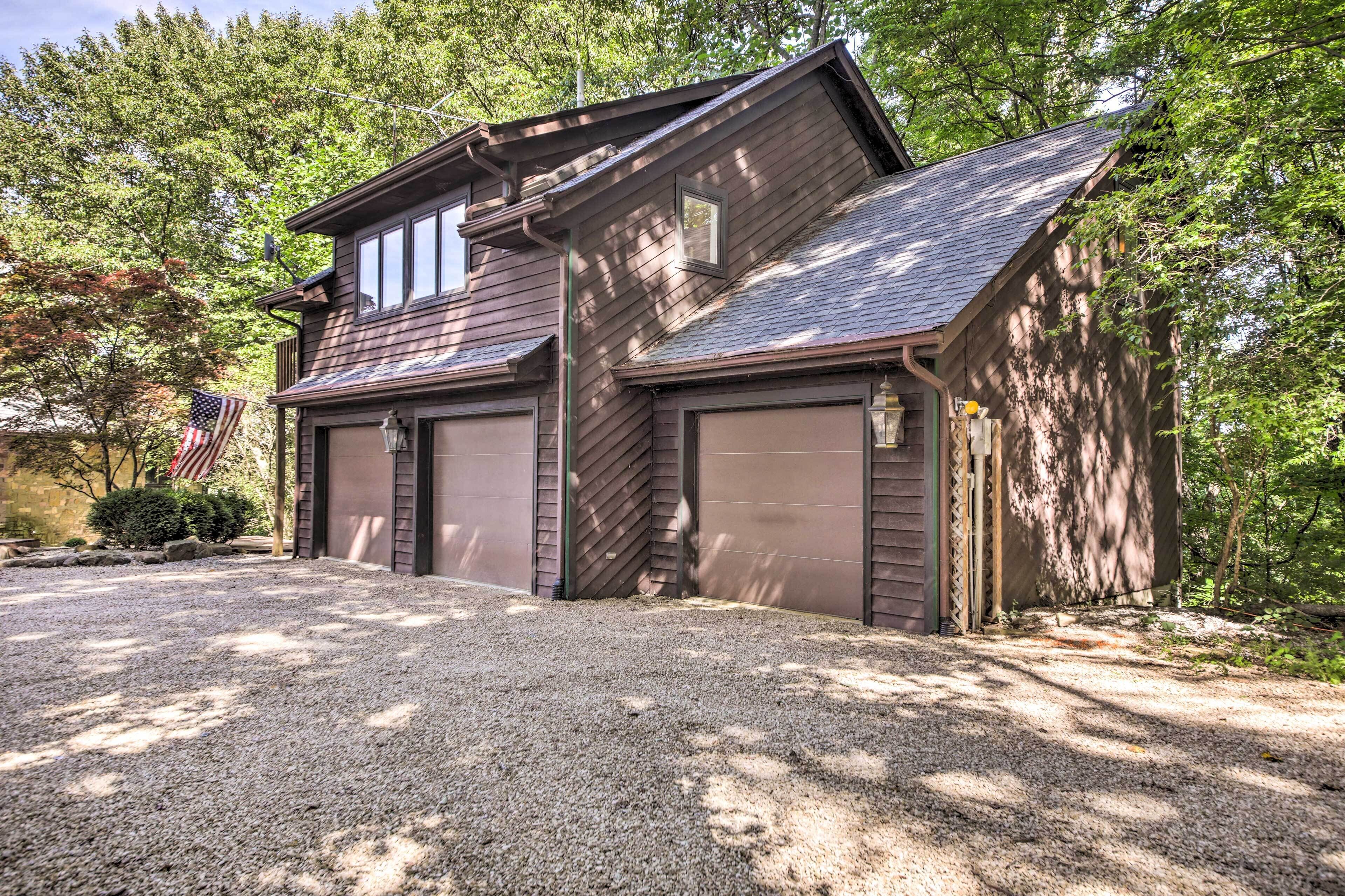 A two-story house with a garage, surrounded by trees and a gravel driveway.