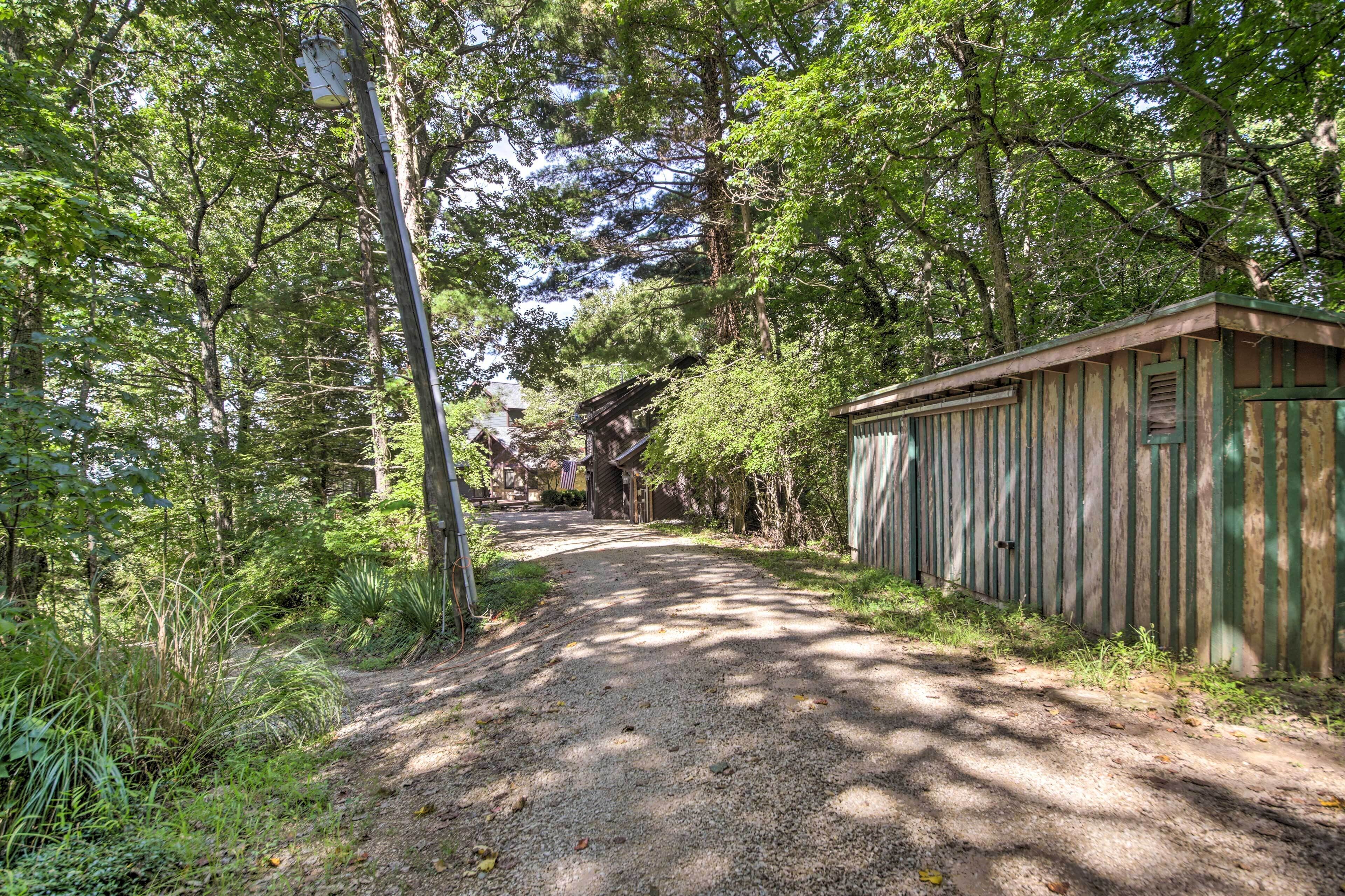 Un sentier de gravier traverse une zone boisée, et une structure en bois rustique se trouve sur la droite.