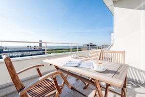 A wooden table with chairs on a balcony overlooking a coastal area. - Penthouse im Haus Wiking - Penthouse. Strand. Citynah - Stw/508 (Sylt)