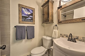 Une salle de bain équipée de toilettes, d’un lavabo et d’un tableau représentant un paysage de montagne.