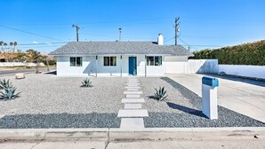 A single-story house with a grey roof, white exterior walls, and a blue door. There is a gravel driveway leading to the front door, and a mailbox is visible on the right side. - < 4 Mi to Dtwn Palm Springs: Home w/ Private Patio (Palm Springs)