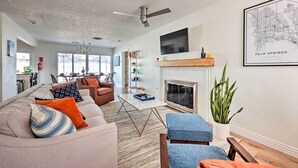 A modern living room with a fireplace, a ceiling fan, and a large TV mounted on the wall. - < 4 Mi to Dtwn Palm Springs: Home w/ Private Patio (Palm Springs)