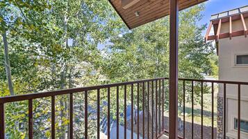 A wooden balcony with a metal railing overlooking a landscaped area with trees and a building in the background.