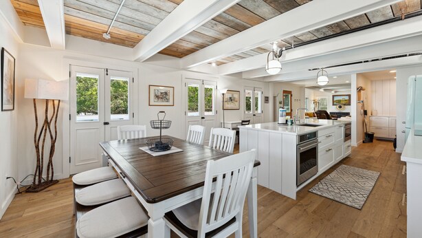 Une cuisine spacieuse avec des meubles blancs, un îlot central en bois et un coin repas doté de chaises blanches.
