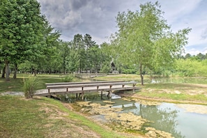 A wooden bridge over a pond with lily pads, surrounded by trees and a pavilion. - The Chalet at Kudzu Cove Cabins Resort (Guntersville)