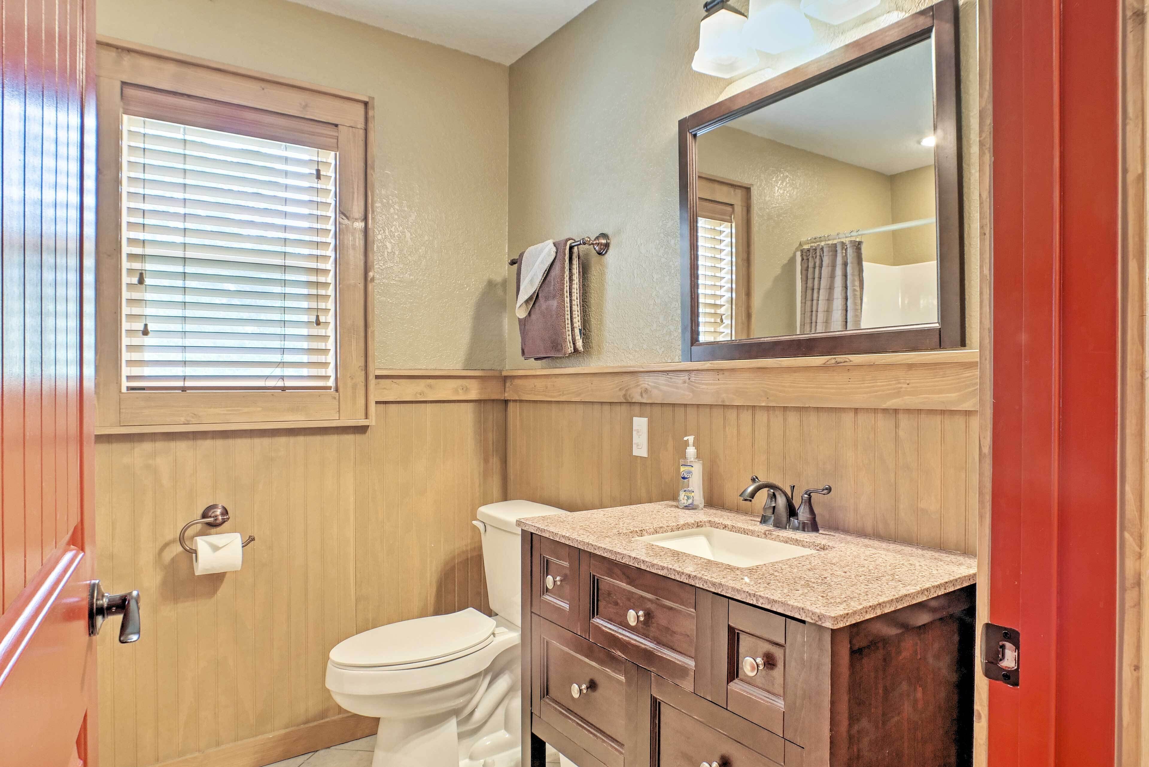 Une salle de bain avec un meuble-lavabo en bois, un évier, un miroir, des toilettes et une fenêtre avec des stores.