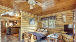 A log cabin interior with a bed, a dining table, a television, and a mounted deer head. - Jemez Springs Cabin w/ Stunning Mtn Views! (Jemez Springs)