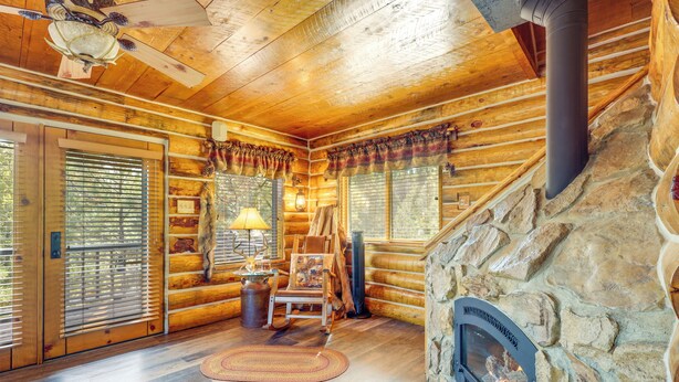 A log cabin interior with a stone fireplace, wooden floors, and a ceiling fan. - Jemez Springs Cabin w/ Stunning Mtn Views! (Jemez Springs)