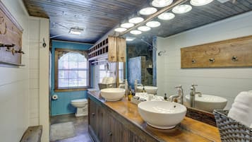 A bathroom with wooden vanity, two sinks, a window, and a mirror.