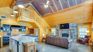 A spacious living area with a stone fireplace, wooden staircase, and a large island with kitchen appliances. - Angler's Cabin: Direct Lake Fork Access, By Marina (Alba)