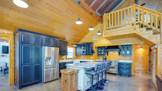 A spacious kitchen with a central island, dark cabinets, stainless steel appliances, and a wooden staircase. - Angler's Cabin: Direct Lake Fork Access, By Marina (Alba)