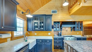A kitchen with wooden walls, dark cabinets, a stainless steel dishwasher, and a large island with a marble countertop. - Angler's Cabin: Direct Lake Fork Access, By Marina (Alba)