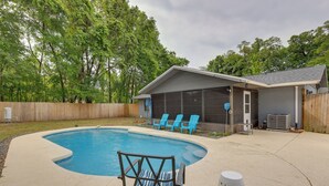A backyard with a swimming pool, a covered patio area, and a wooden fence. - Charming Ocala Home Near World Equestrian Center! (Ocala)