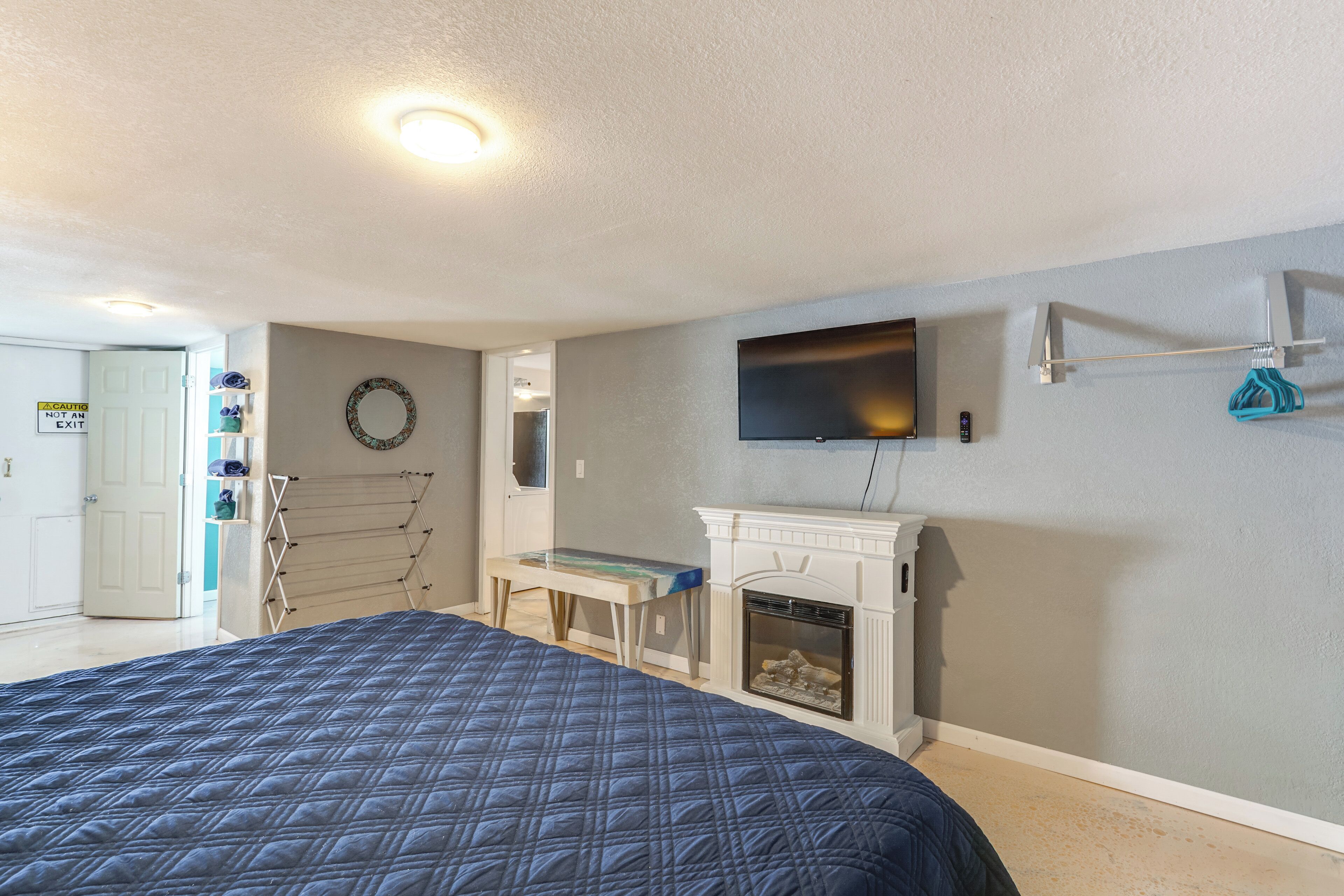 A bedroom with a bed, a TV mounted on the wall, a fireplace, and a door with a sign indicating it's not an exit.
