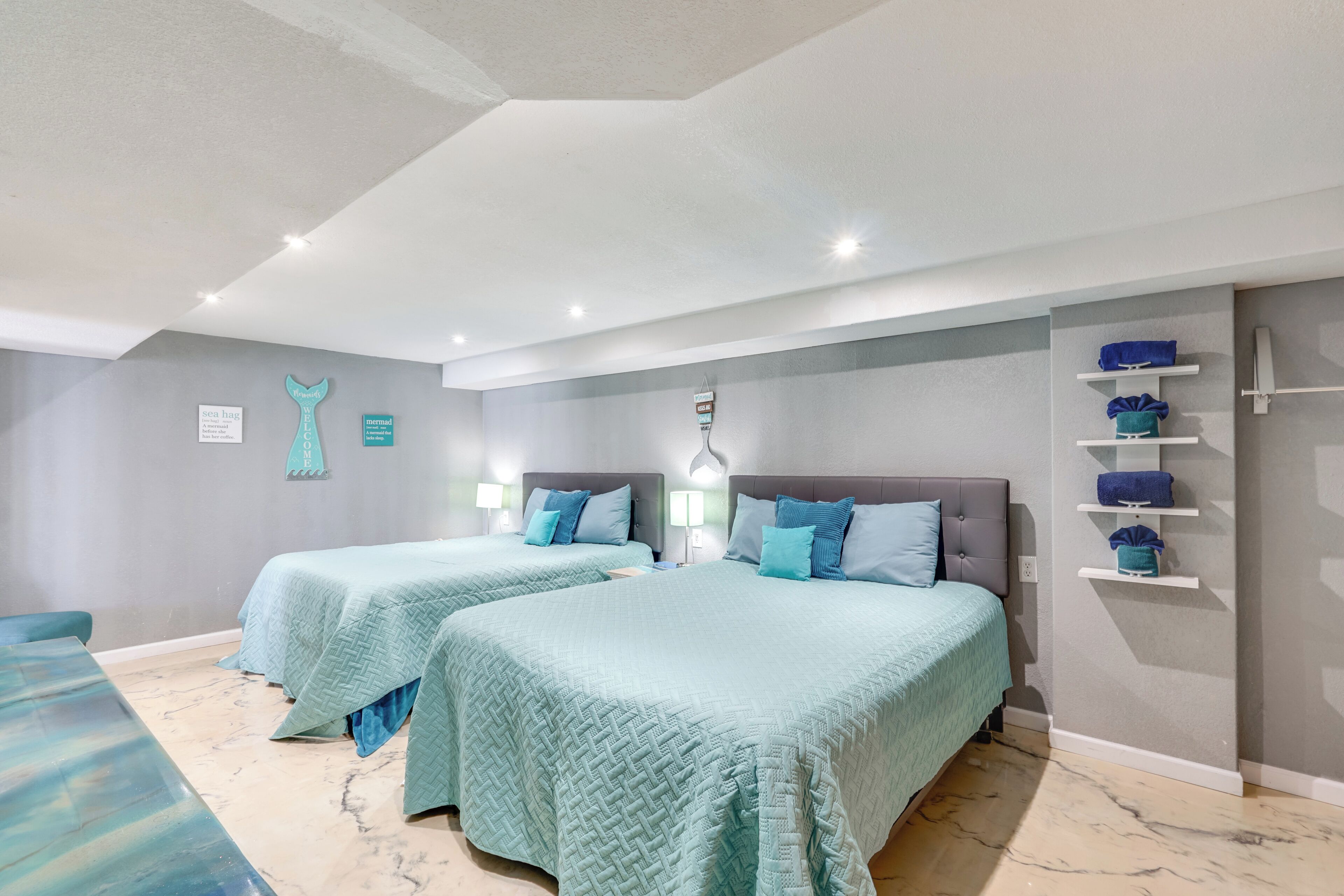 Habitación de hotel con dos camas, suelo de mármol y estante en la pared con toallas.