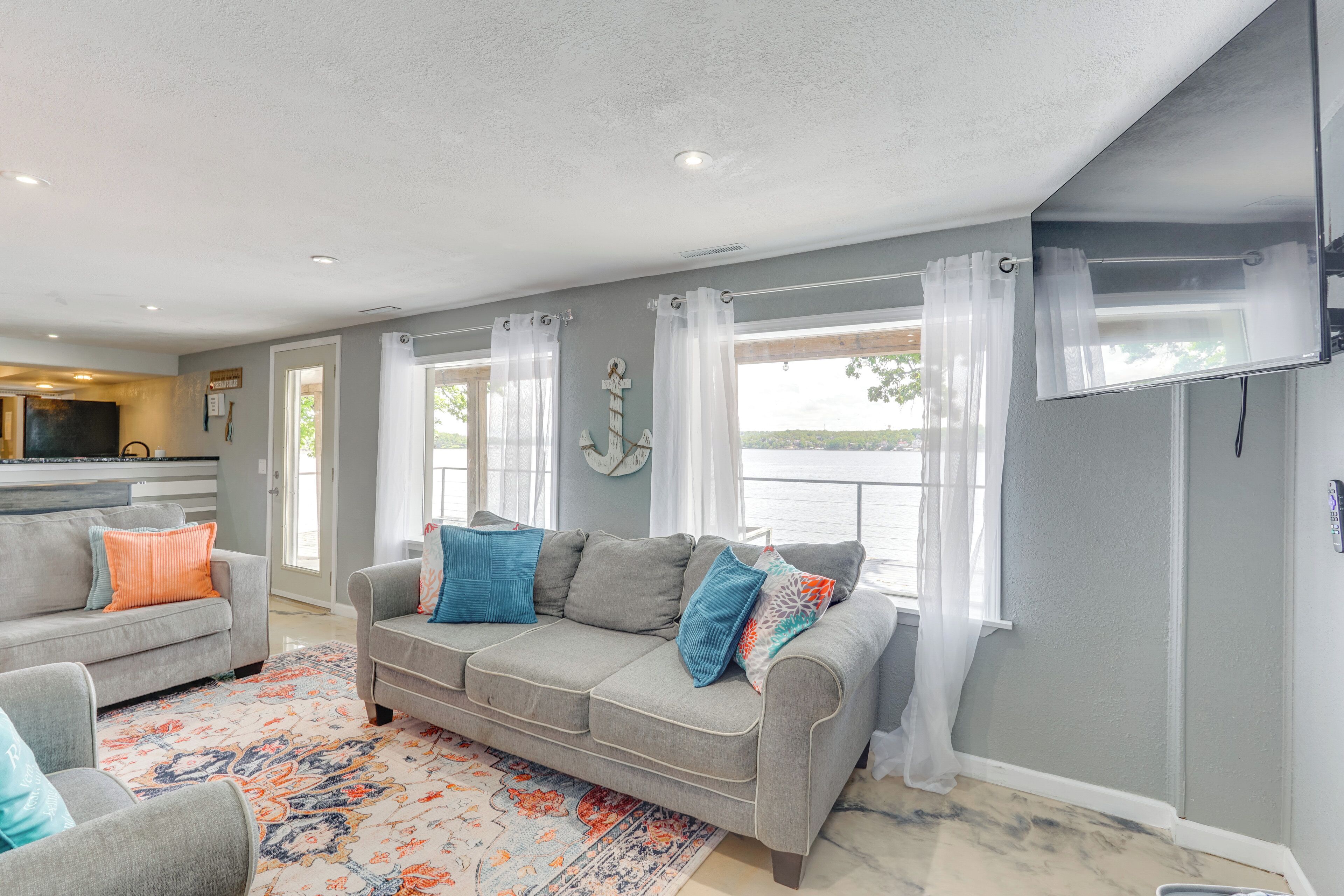 A living room with two grey sofas, a patterned rug, and a view of a body of water through large windows.