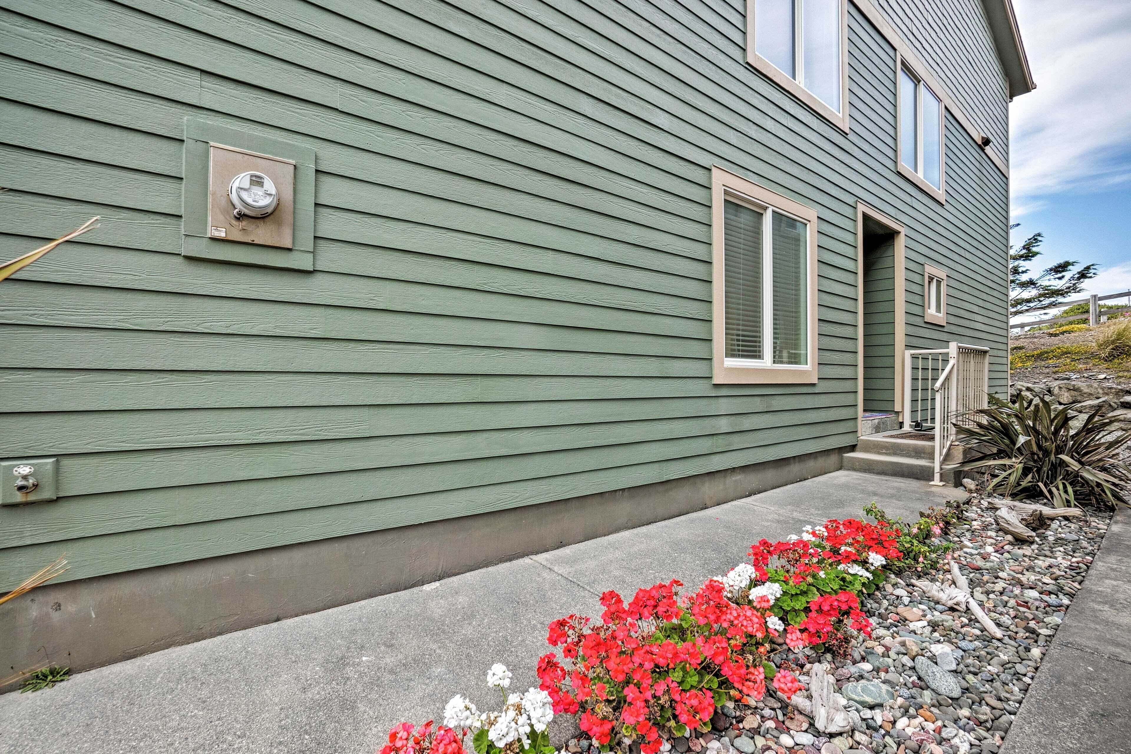 A green house with a small porch and a flower bed with red and white flowers.
