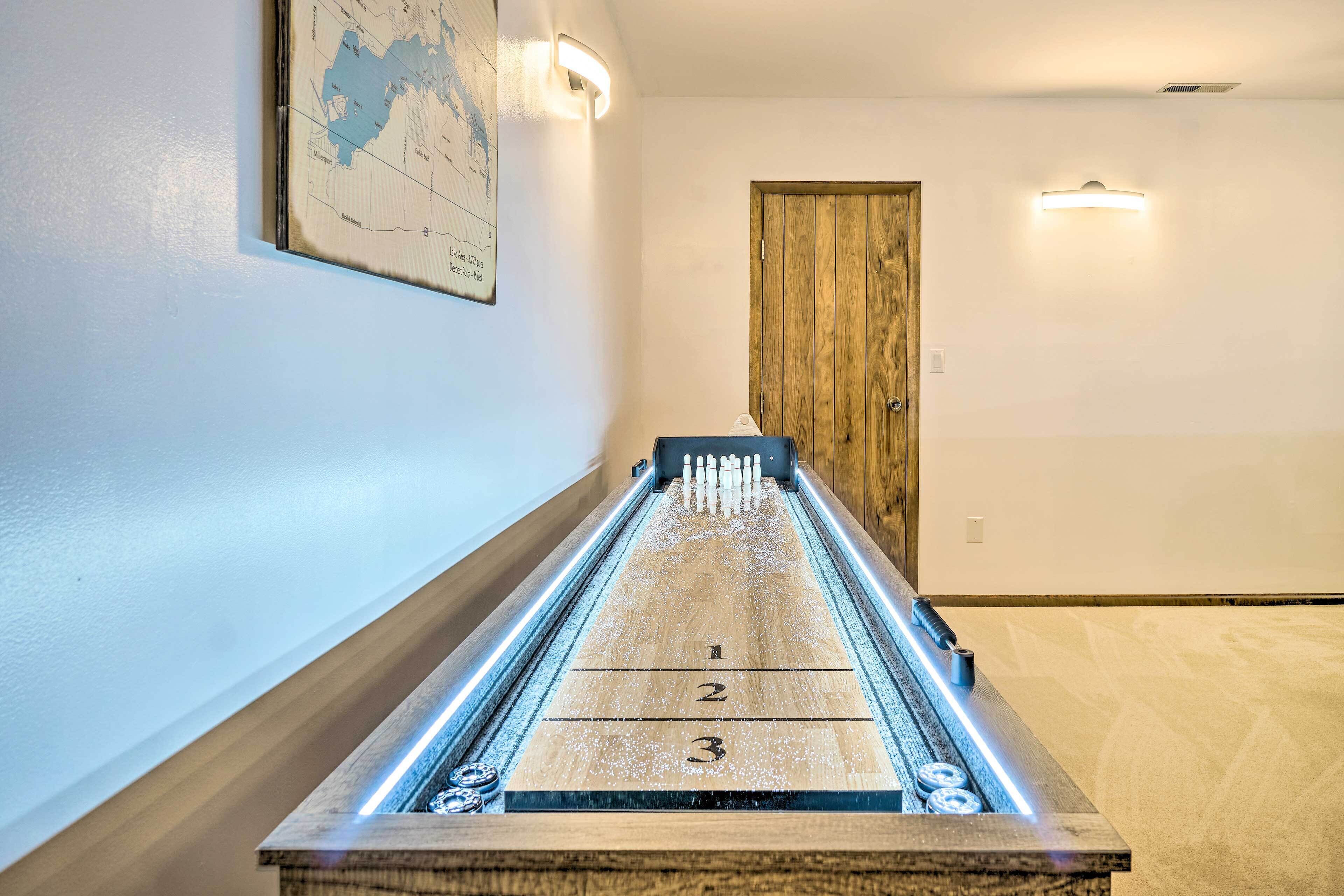 A shuffleboard table with illuminated edges, a wooden door, and a map on the wall.