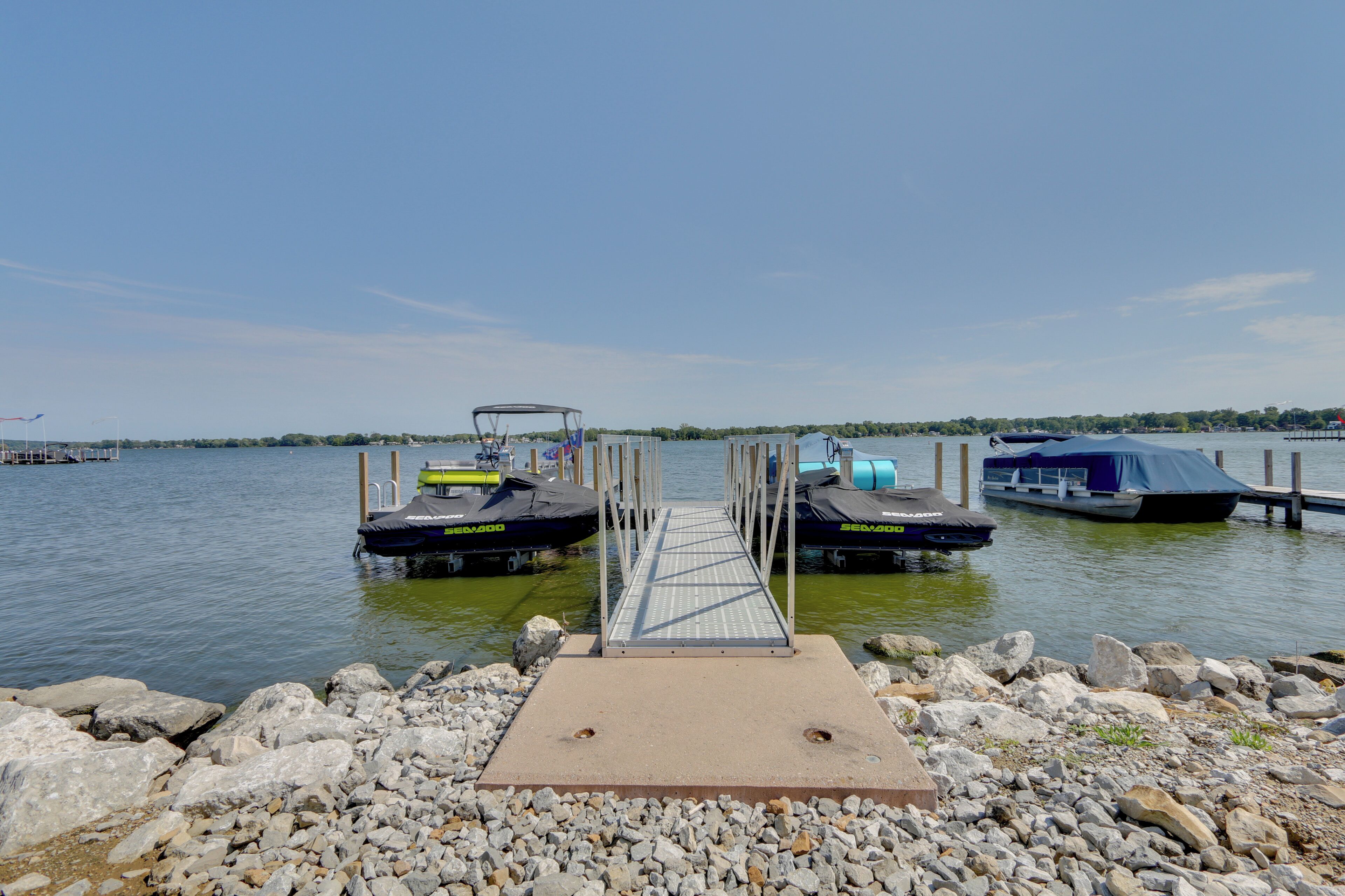 A dock with a metal walkway leading to two boats, surrounded by rocks and calm water.