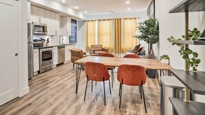 A modern kitchen with white cabinets, stainless steel appliances, and a wooden dining table with orange chairs. - Trendy Apt w/ Laundry Machines < 3 Mi to Dtwn (Philadelphia)