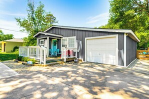 A single-story building with a garage, a porch with a railing, and a small garden area. - Pet-friendly Cottage, 3 Blocks to Main St! (Tomball)