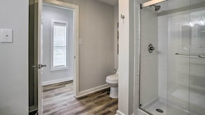 A bathroom with a glass shower enclosure, a toilet, and a door leading to another room. - Pet-friendly Cottage, 3 Blocks to Main St! (Tomball)