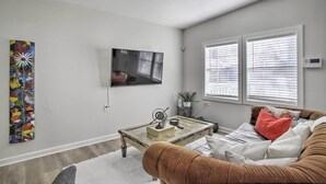 A living room with a television mounted on the wall, a coffee table with decorative items, a sofa with cushions, and a colorful abstract painting. - Pet-friendly Cottage, 3 Blocks to Main St! (Tomball)