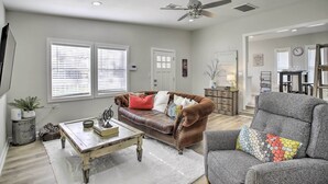 A spacious living room with a brown leather couch, a gray armchair, and a wooden coffee table. There is a ceiling fan, a fireplace, and a dining area in the background. - Pet-friendly Cottage, 3 Blocks to Main St! (Tomball)