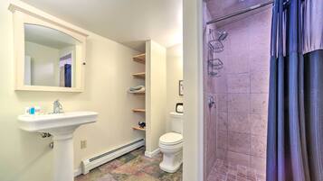 A bathroom with a pedestal sink, a toilet, a shower with a glass door, and a mirror. Shelves are mounted on the wall above the toilet.