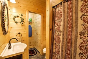 Een houten badkamer in een vakantiehuis, met een wastafel, toilet en douchegordijn.