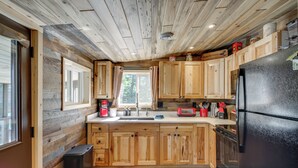 A kitchen with wooden cabinets, a black refrigerator, and a window with curtains. - Pequot Lakes Cabin w/ Dock on Loon Lake! (Pequot Lakes)