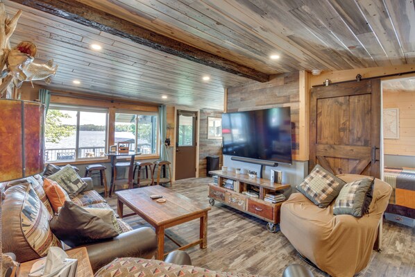 Una sala de estar acogedora con una televisión grande, muebles de madera y vistas al exterior.
