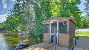 A wooden cabin with a sign reading "The Loon Bin" on a dock by a lake surrounded by trees. - Pequot Lakes Cabin w/ Dock on Loon Lake! (Pequot Lakes)