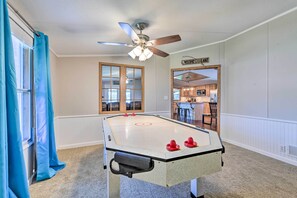 A room with a foosball table, a ceiling fan, and a kitchen area visible through an open door. - Lakefront Granbury Home, Boat Dock On-site! (Granbury)