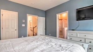 A bedroom with a large bed, a dresser, a TV, and a door leading to a bathroom.