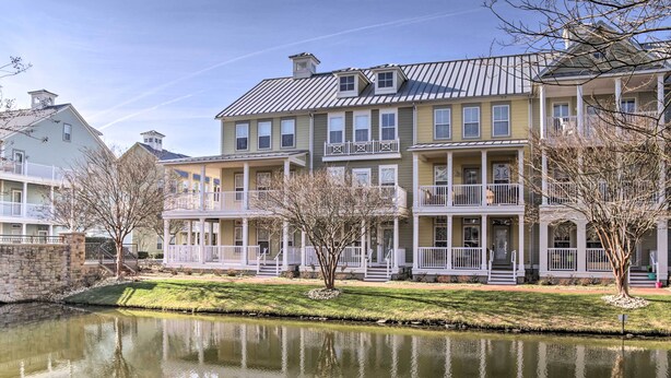 A row of multi-story buildings with balconies, a small pond in the foreground, and a stone wall.
