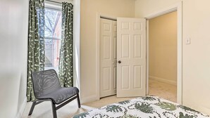 A bedroom with a bed, a chair, a window with curtains, and a closed door. - Philadelphia Home Rental Near Center City! (Philadelphia)
