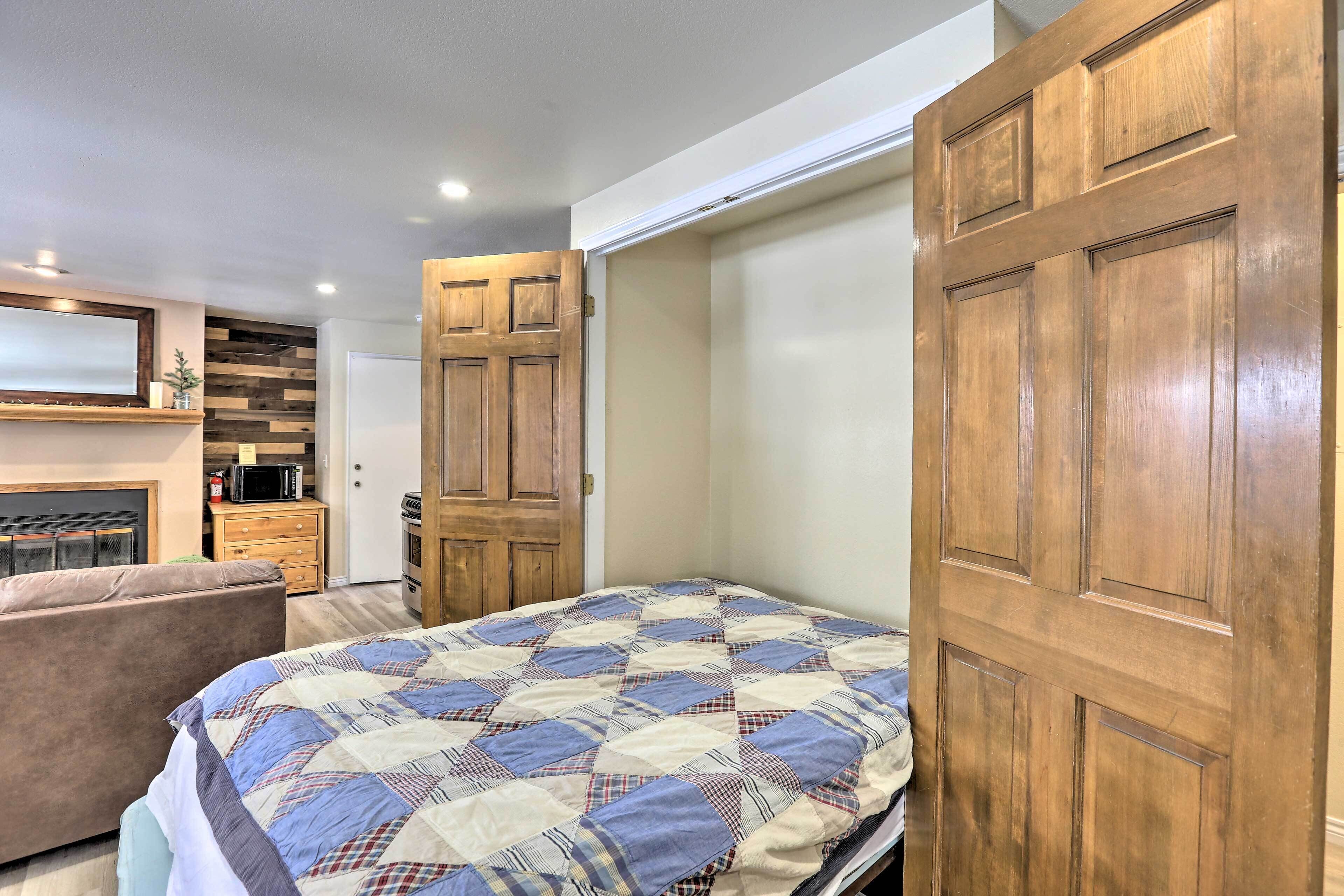 Un dormitorio con cama, armario de madera y una pequeña cocina.