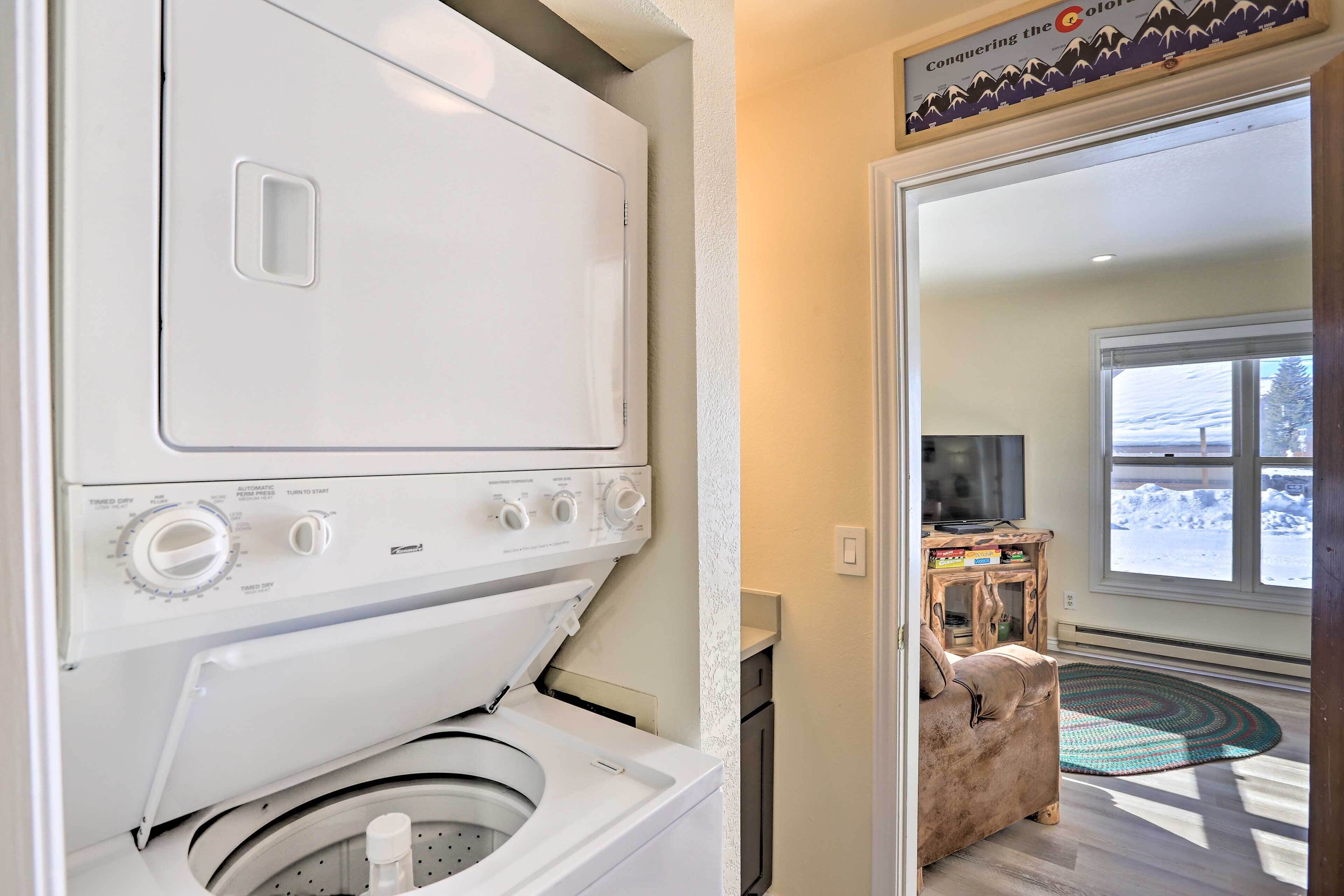 A laundry room with a front-loading washer and dryer, a wooden bench, and a view of a snowy landscape through a window.