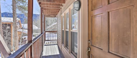 A wooden deck with a railing, a wooden door with a window, and a view of snow-covered houses in the background.