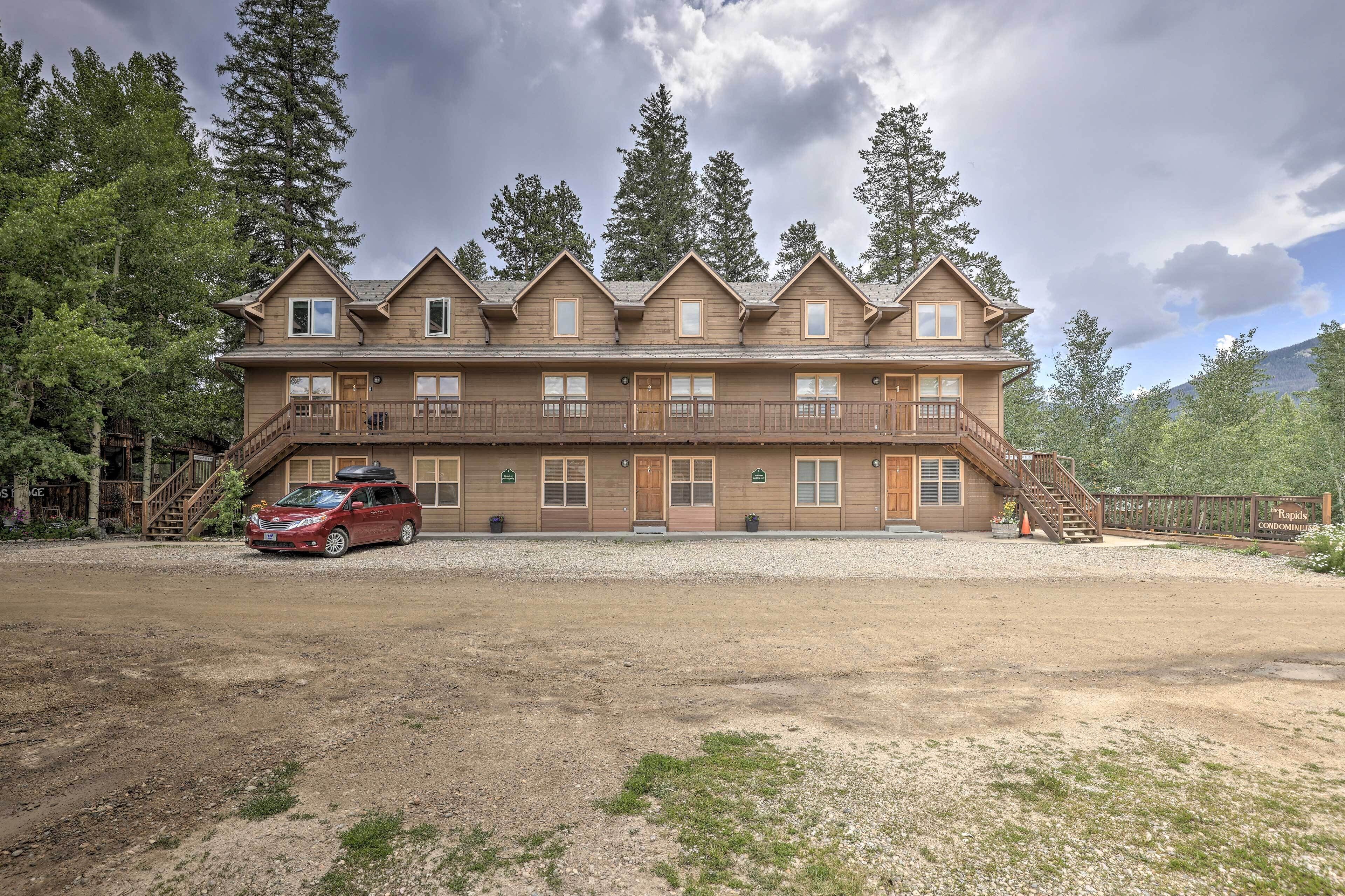 A multi-story wooden building with a covered front porch, a car parked in front, and a mountainous backdrop.