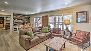 A spacious living room with a brown leather sofa, a wooden coffee table, and a brown leather armchair. There is a dining area with a wooden table and chairs, and a kitchen in the background. - Walk to Marina: Rustic Grand Lake Retreat! (Grand Lake)