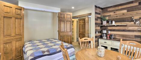 A bedroom with a bed, wooden wardrobe, and a small dining table with chairs.